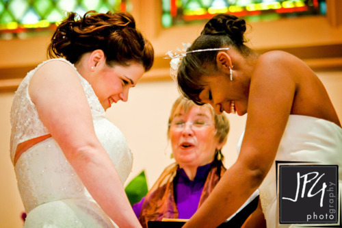 Two women both wearing wedding dresses stand at the altar during their 
