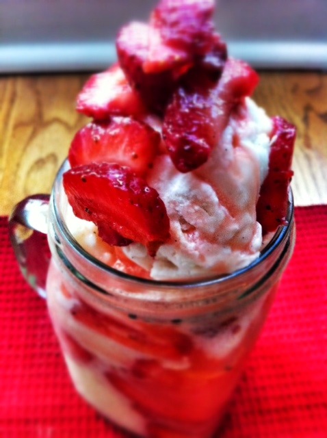 Close up of a glass jar filled with a strawberry ice cream float containing vanilla ice cream topped with fresh, sliced strawberries.