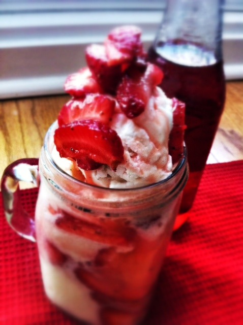 Strawberry float contained in a glass mug with a strawberry soda in the background.
